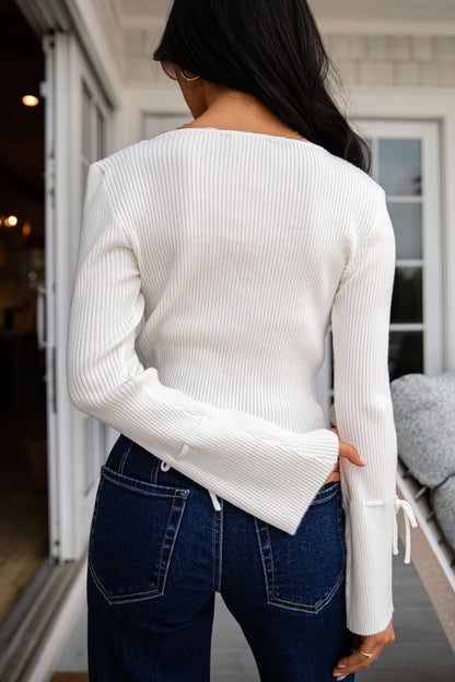 Person wearing a white sweater and blue jeans standing in front of a house.