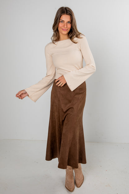 Woman wearing a beige top and brown skirt against a white background
