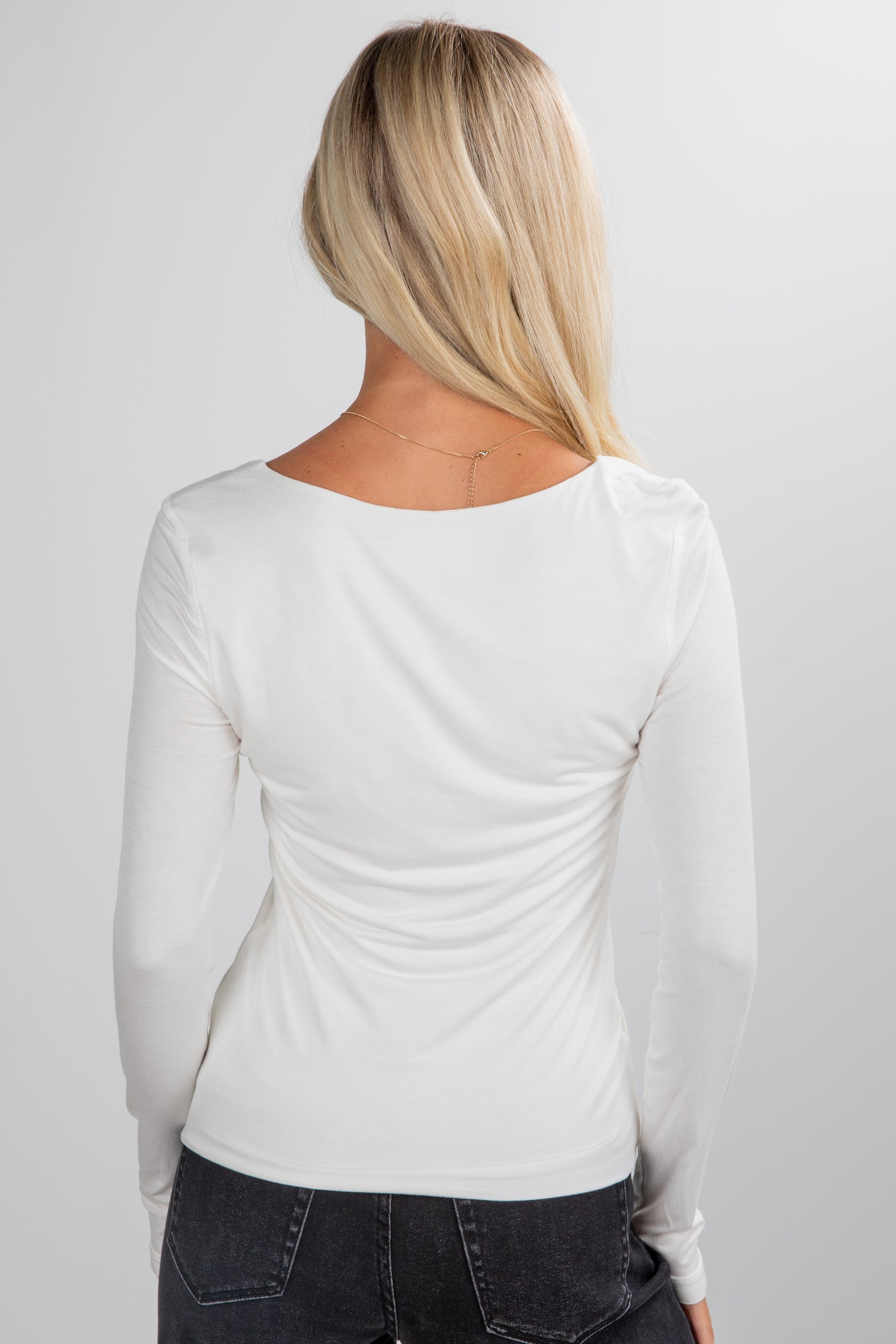 Person wearing a white long-sleeve top and dark jeans on a plain background