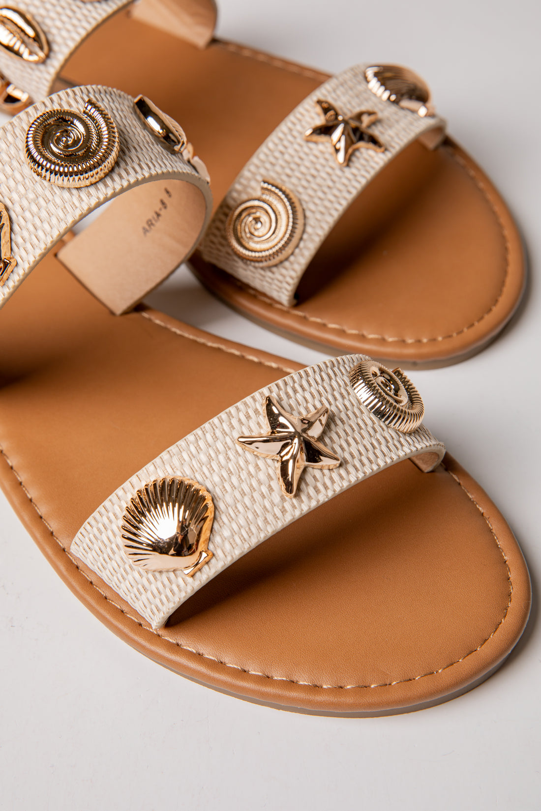 Beige sandals with gold embellishments on a light gray background