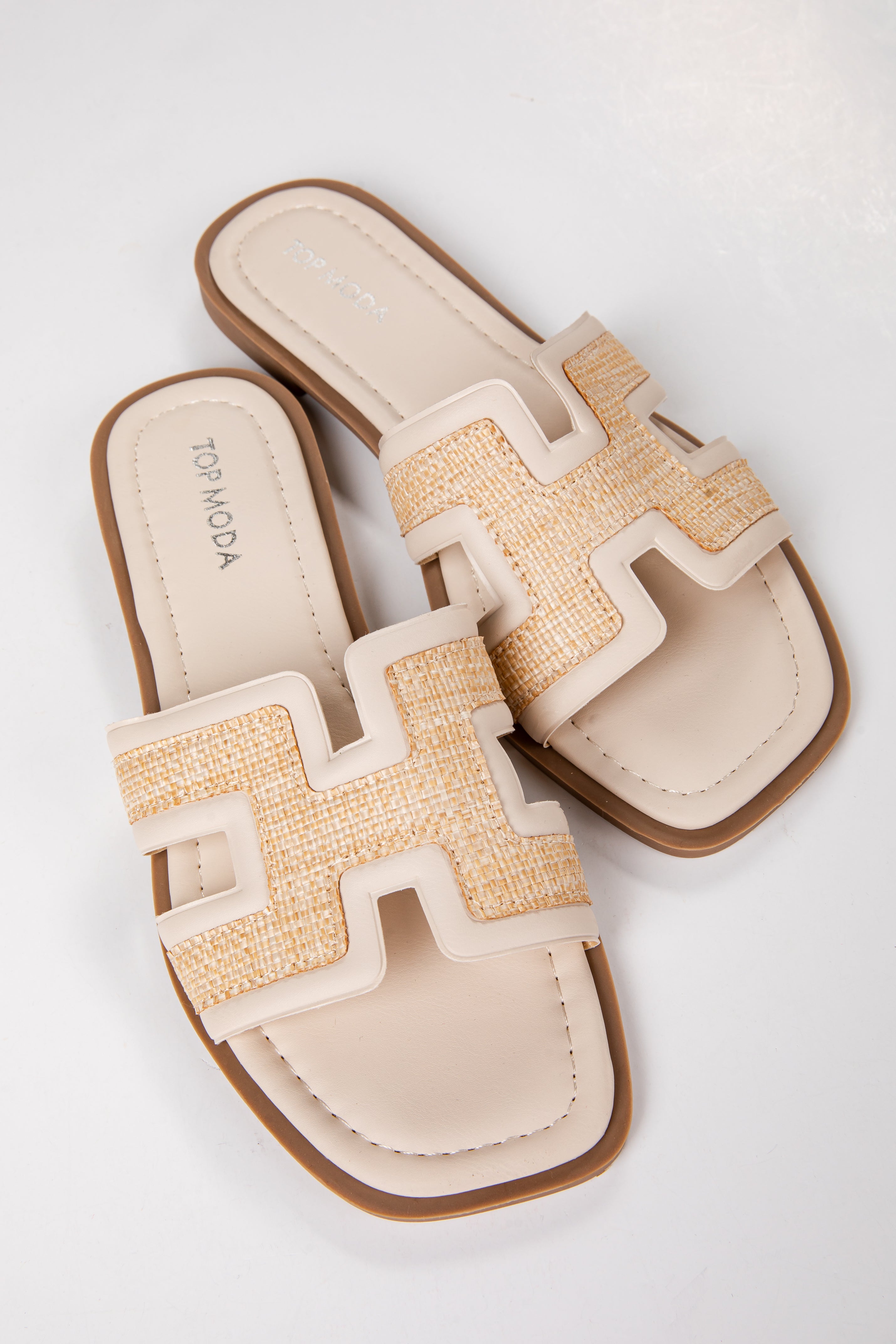 Pair of beige sandals with a textured strap on a white background