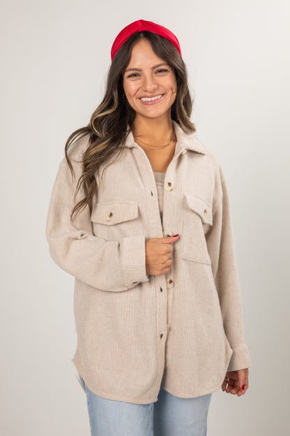 Woman wearing a beige corduroy shirt over a sweater with a red headband on a white background