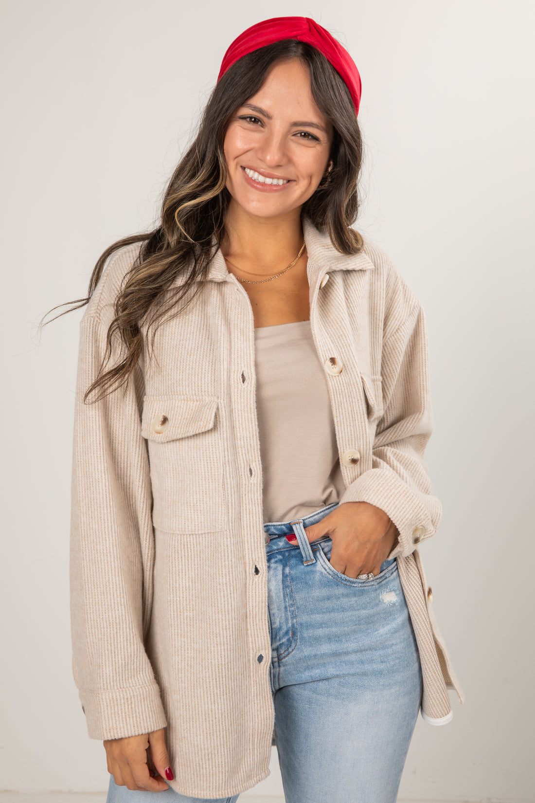 Woman wearing a beige corduroy jacket, red headband, and blue jeans against a plain background
