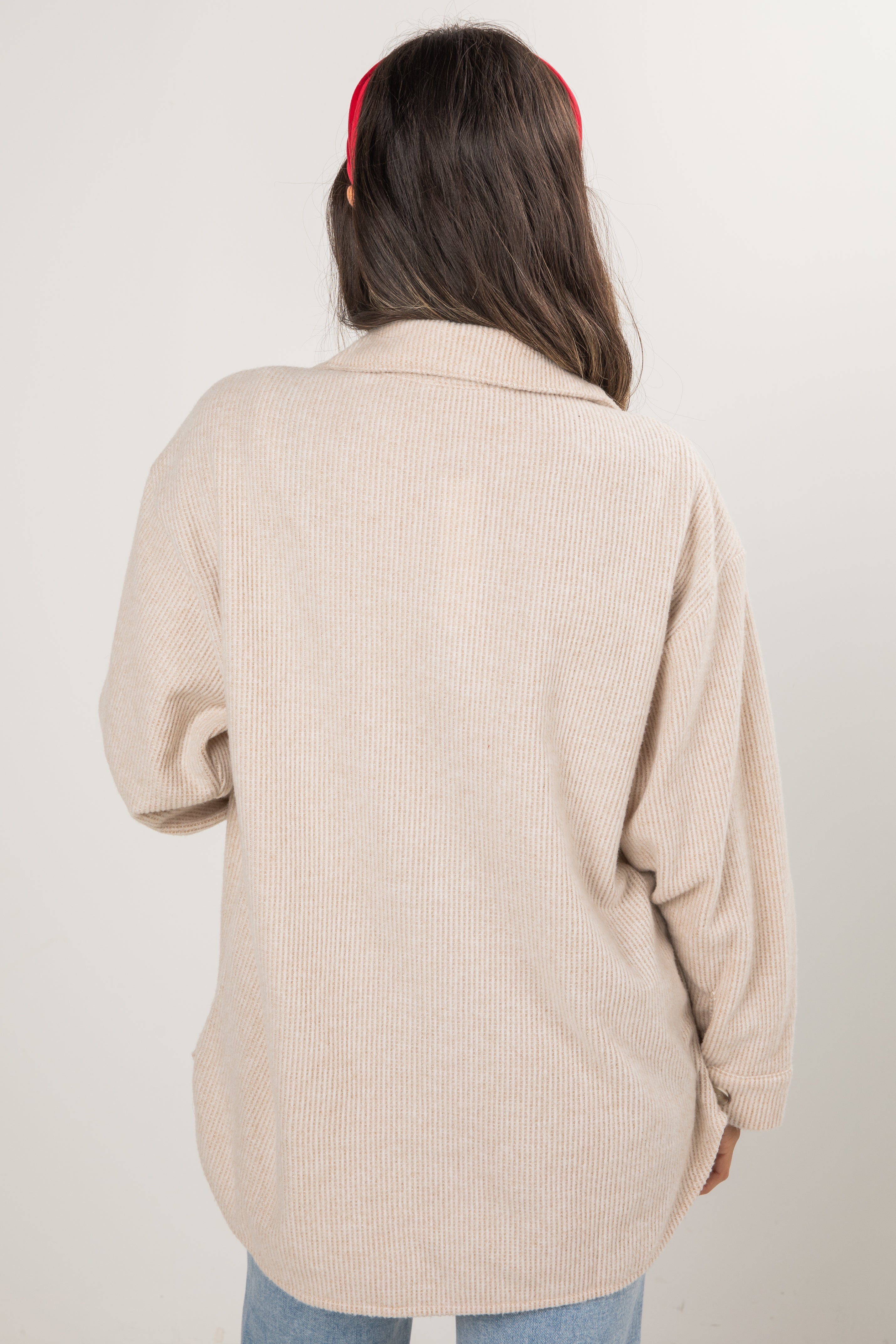 Person wearing a beige ribbed sweater with a plain background