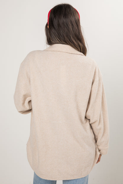 Person wearing a beige ribbed sweater with a plain background