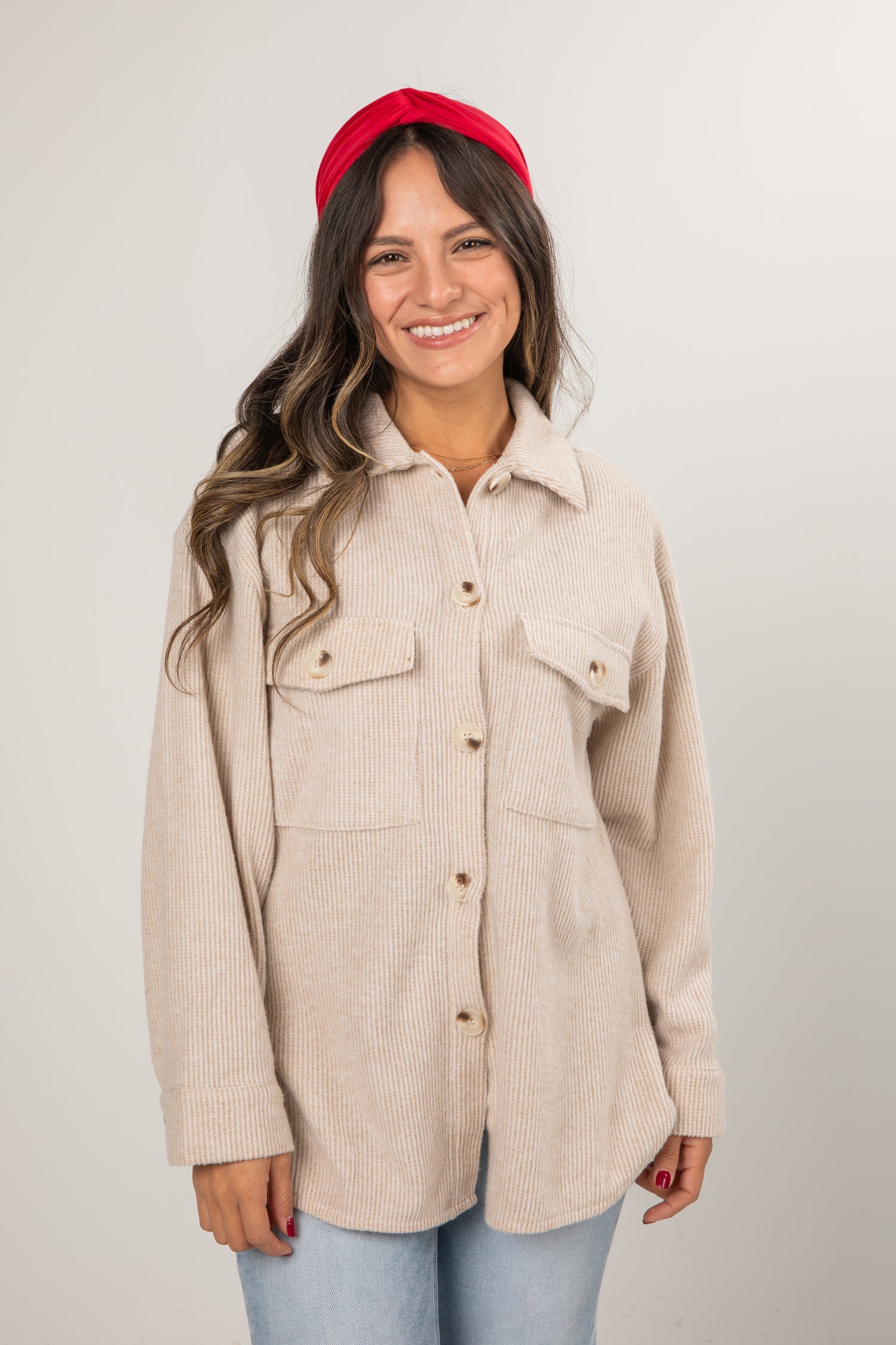 Woman wearing a beige jacket and red headband on a plain background