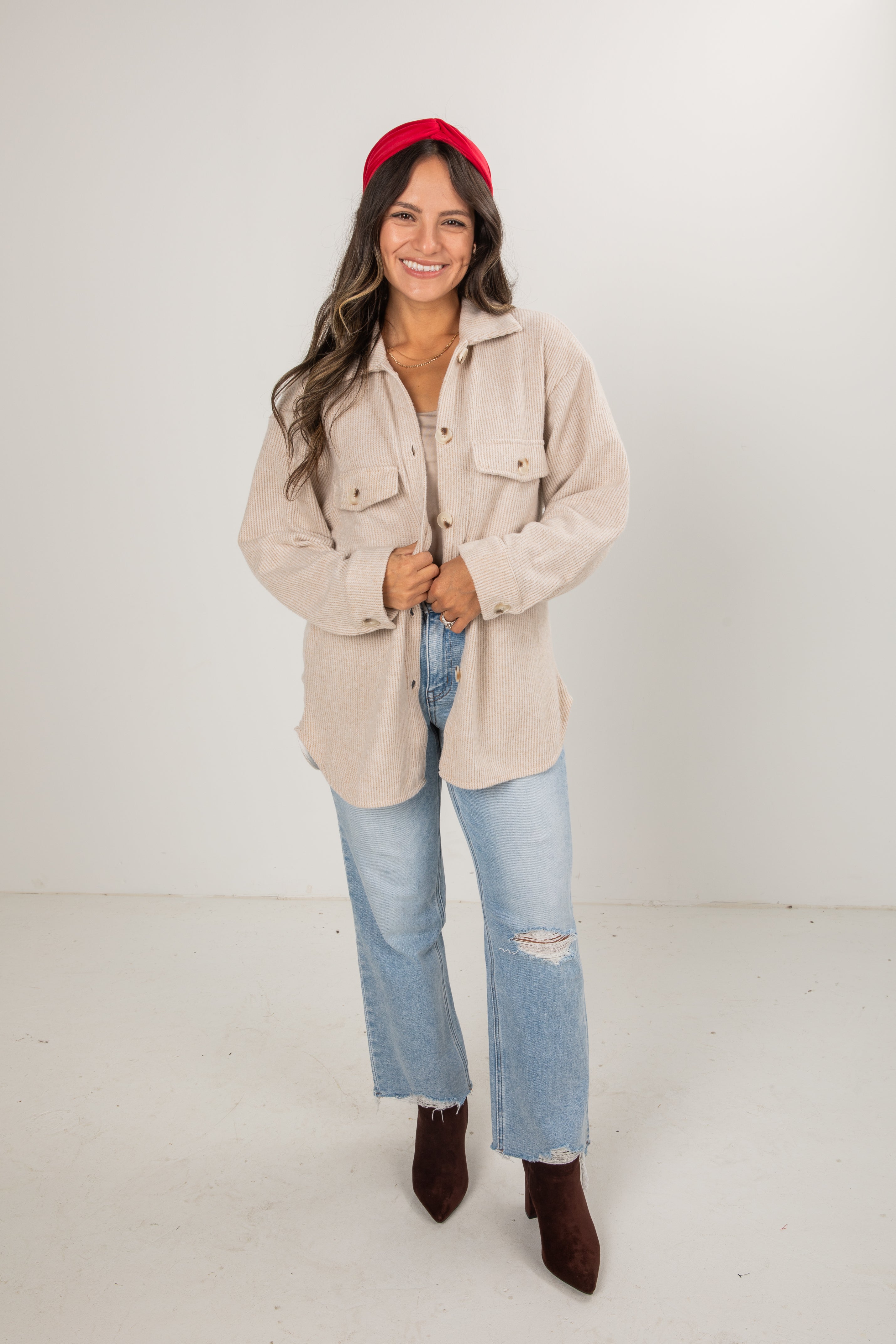 Woman wearing a beige jacket, red beanie, blue jeans, and brown boots on a white background