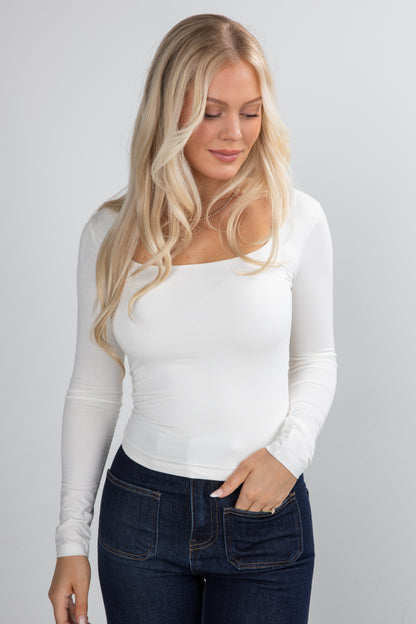 Woman wearing a white long-sleeve top and dark jeans on a gray background