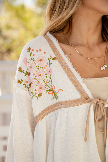 Woman wearing a white embroidered cardigan with floral designs outdoors.