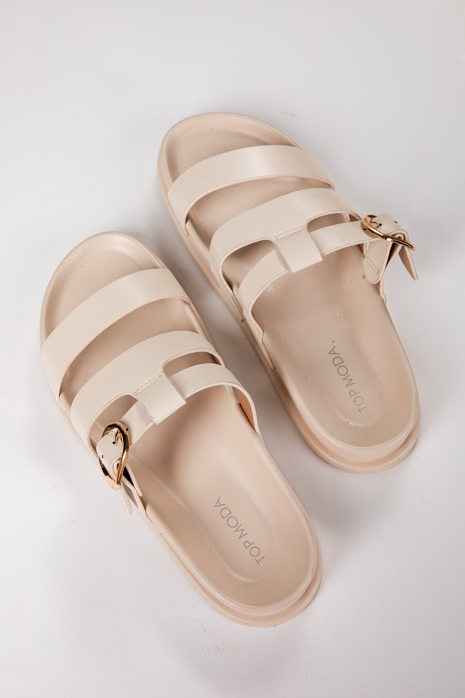 Pair of beige sandals with gold buckles on a light gray background