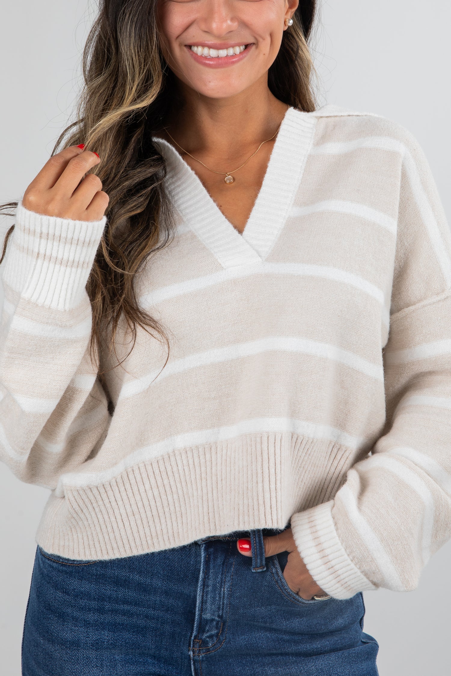 Woman wearing a cream and beige striped sweater with blue jeans on a white background