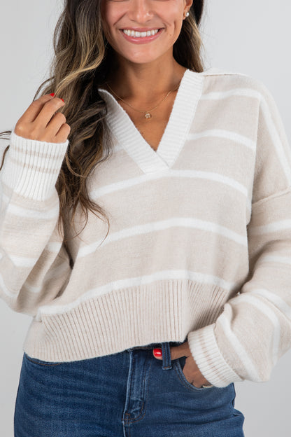 Woman wearing a cream and beige striped sweater with blue jeans on a white background
