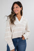 Woman wearing a cream striped sweater and blue jeans against a white background