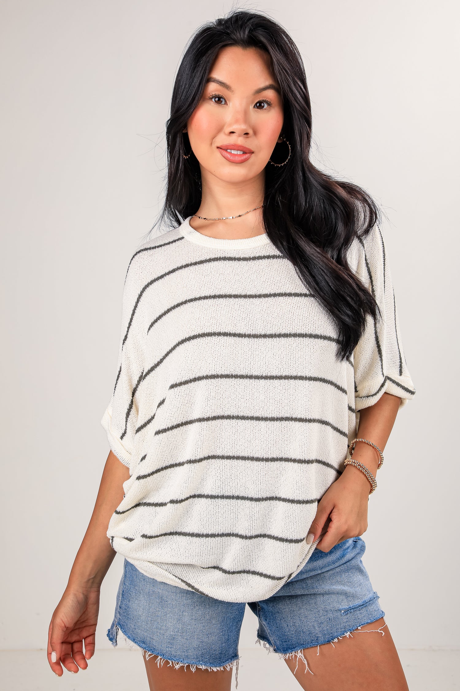 Woman wearing a striped sweater and denim shorts against a plain background