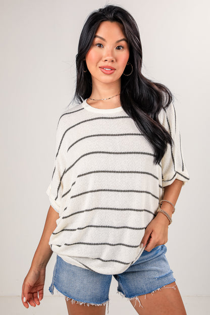 Woman wearing a striped sweater and denim shorts against a plain background
