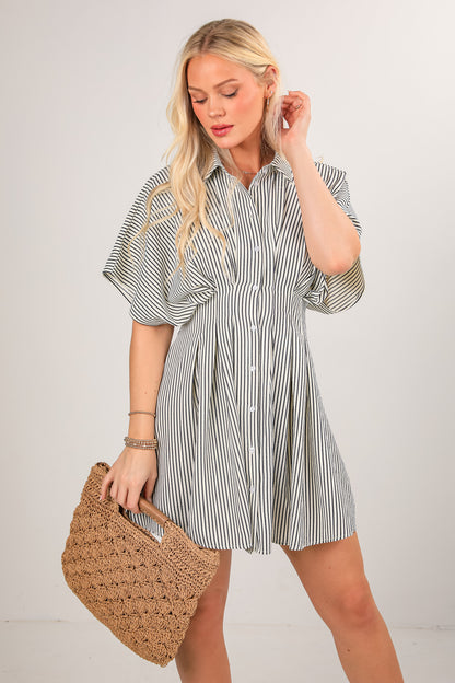 Woman wearing a striped shirt dress holding a woven bag against a plain background
