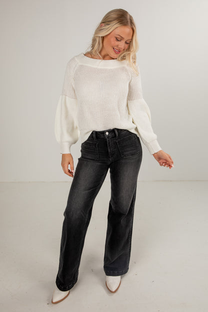 Woman wearing a white sweater and black jeans on a plain background
