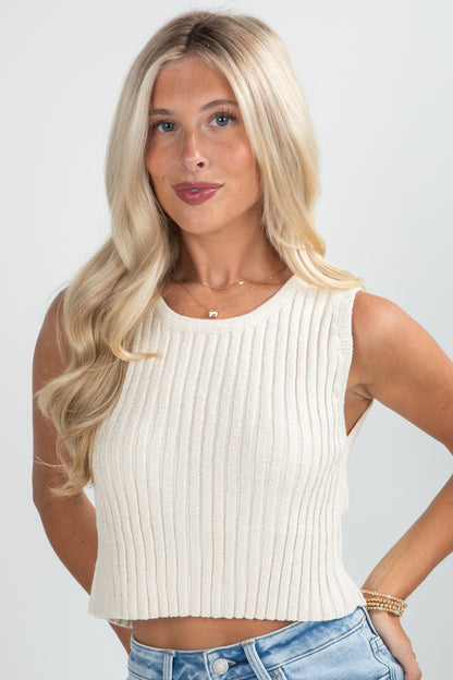 Woman wearing a white ribbed tank top and blue jeans against a plain background