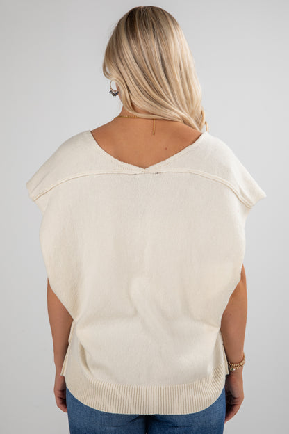 Person wearing a beige sweater vest on a plain background