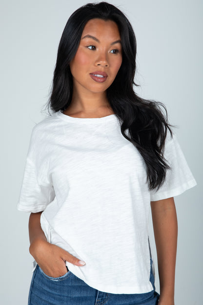 Woman wearing a white t-shirt and blue jeans against a gray background