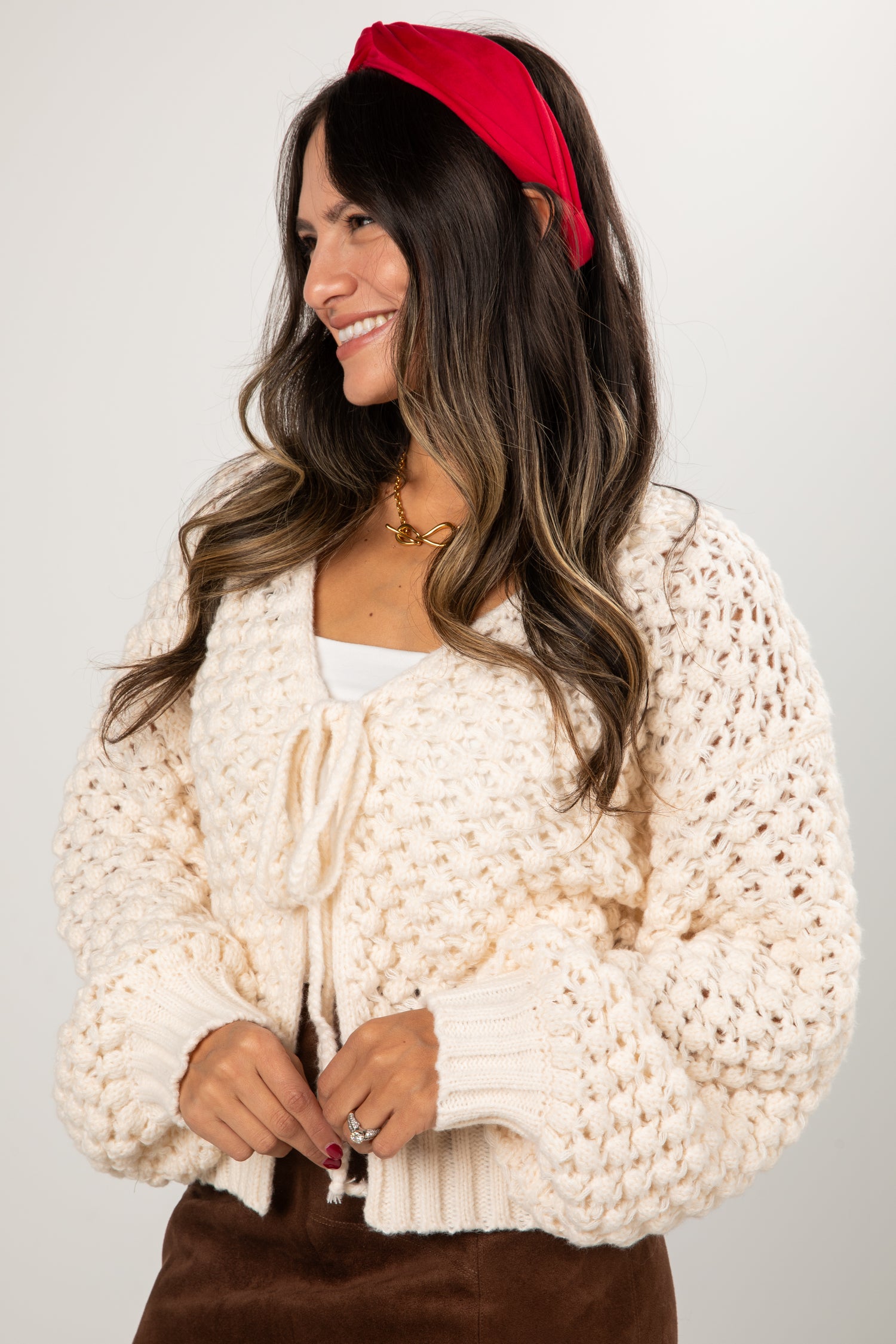 Woman wearing a cream chunky knit cardigan and red headband on a plain background