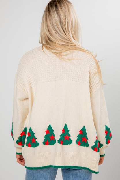 Person wearing a cream sweater with Christmas tree patterns on a plain background