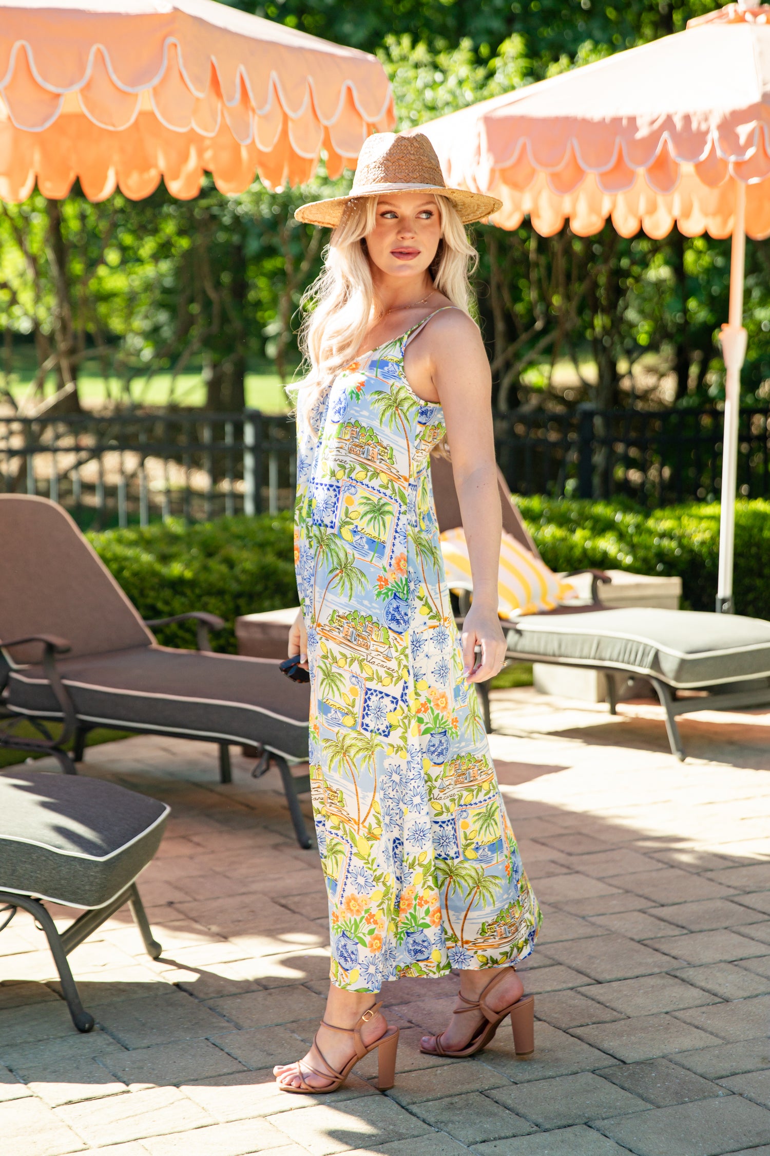 Woman in a floral dress standing under orange umbrellas in a garden setting
