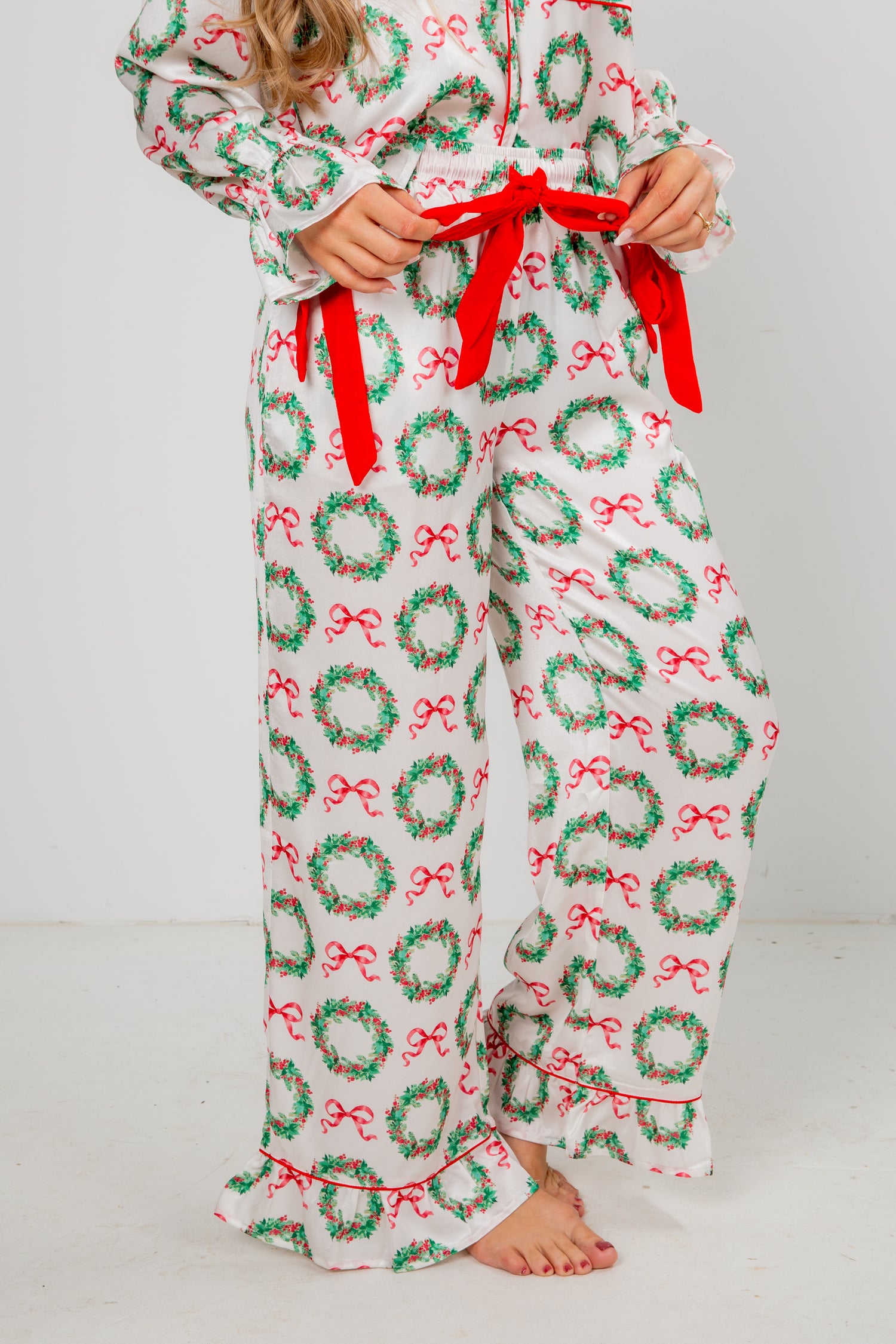 Person wearing a festive pajama set with wreath and bow pattern on a plain background