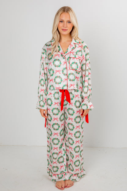 Woman wearing a festive pajama set with wreath and bow pattern on a plain background