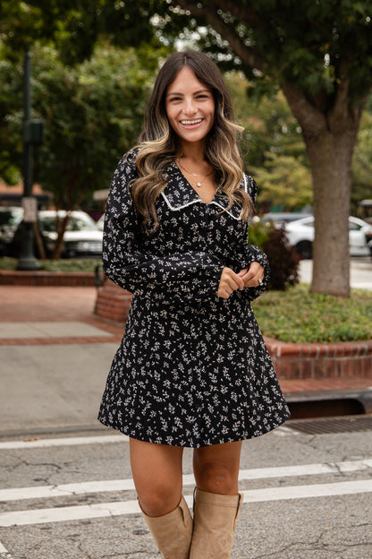 Woman in a black floral dress with beige knee-high boots standing on a street.