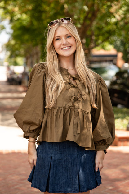 Woman wearing a brown blouse and blue skirt outdoors with trees in the background