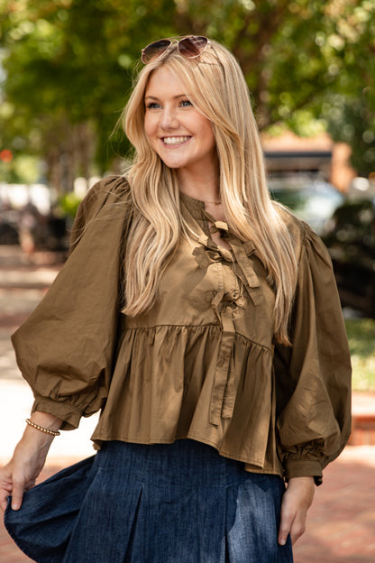 Woman wearing a brown blouse and blue skirt outdoors with trees in the background