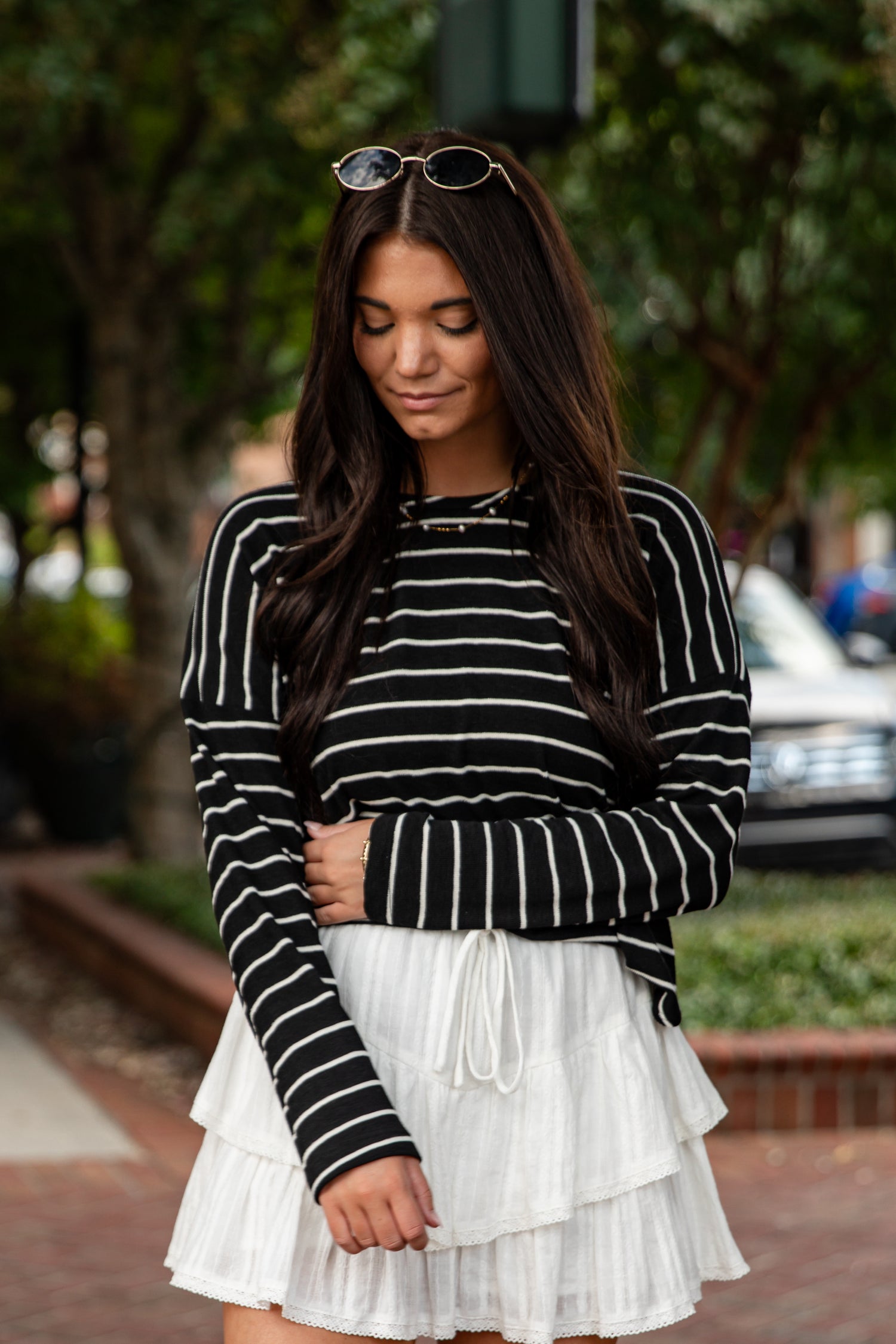 Woman wearing a black and white striped sweater and white skirt outdoors.