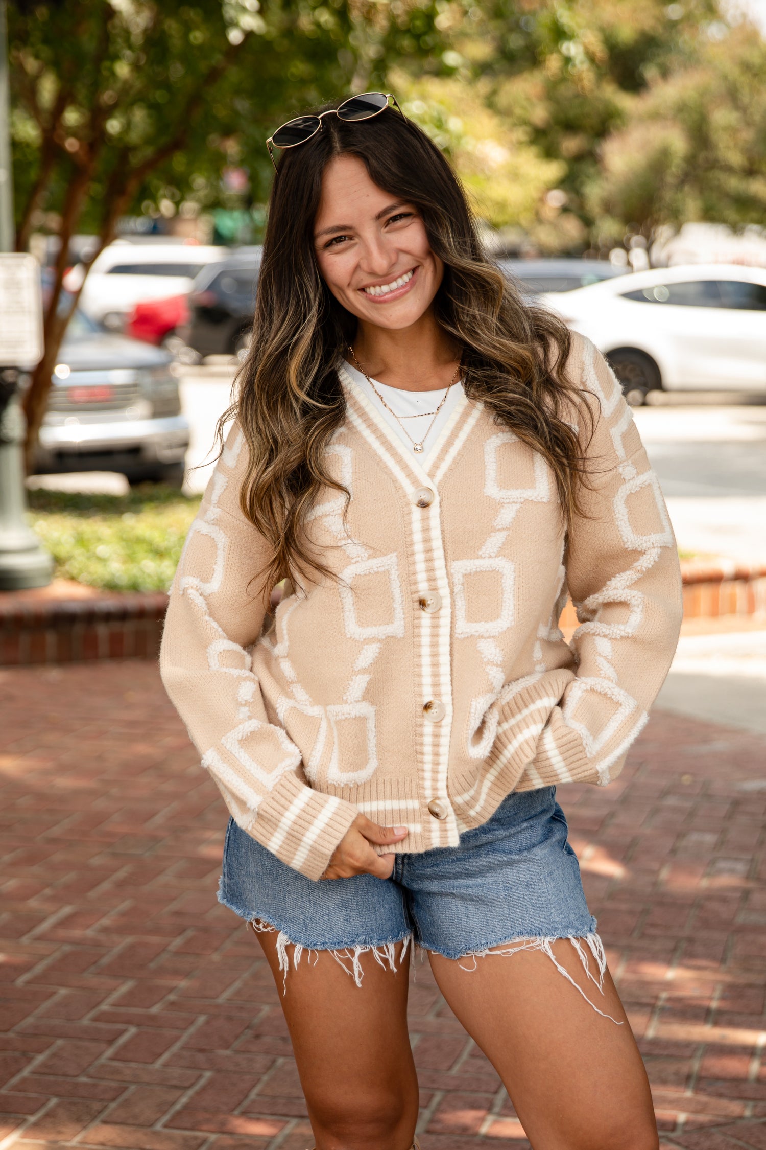 Woman wearing a patterned cardigan and denim shorts standing outdoors.