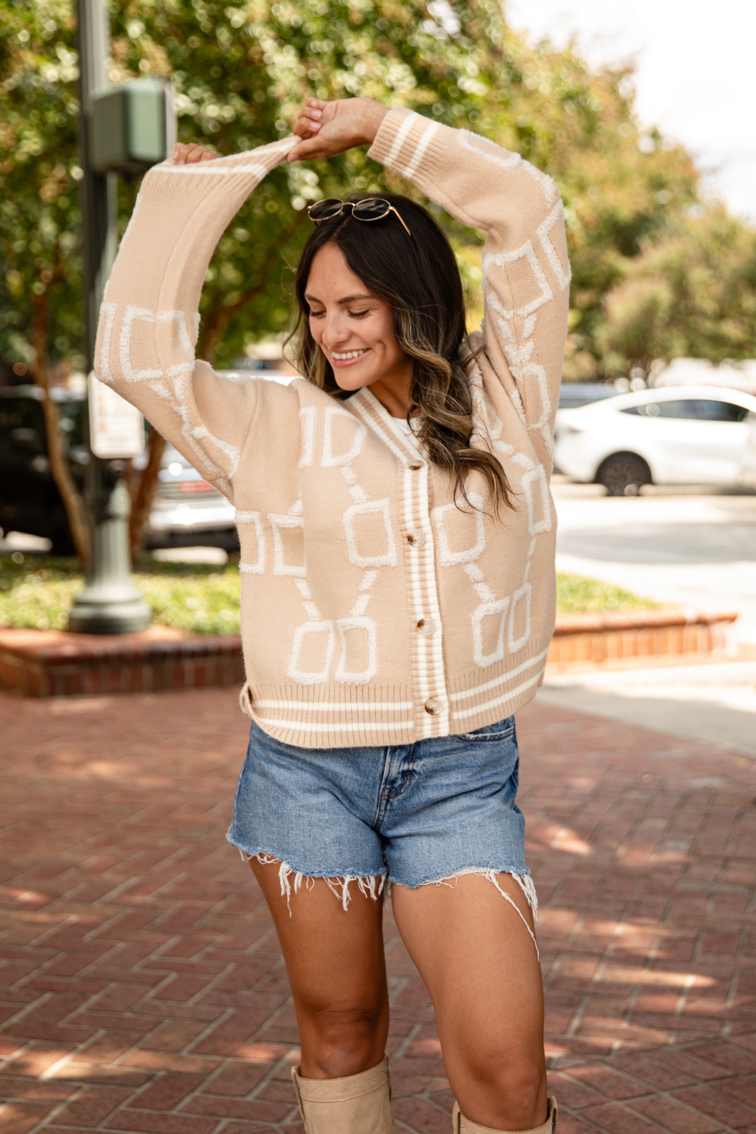 Woman wearing a beige patterned cardigan and denim shorts outdoors.