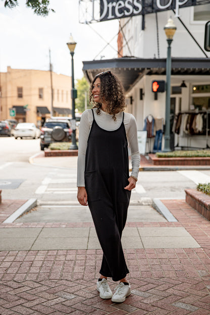 Woman in black jumpsuit and gray cardigan standing on a city street.