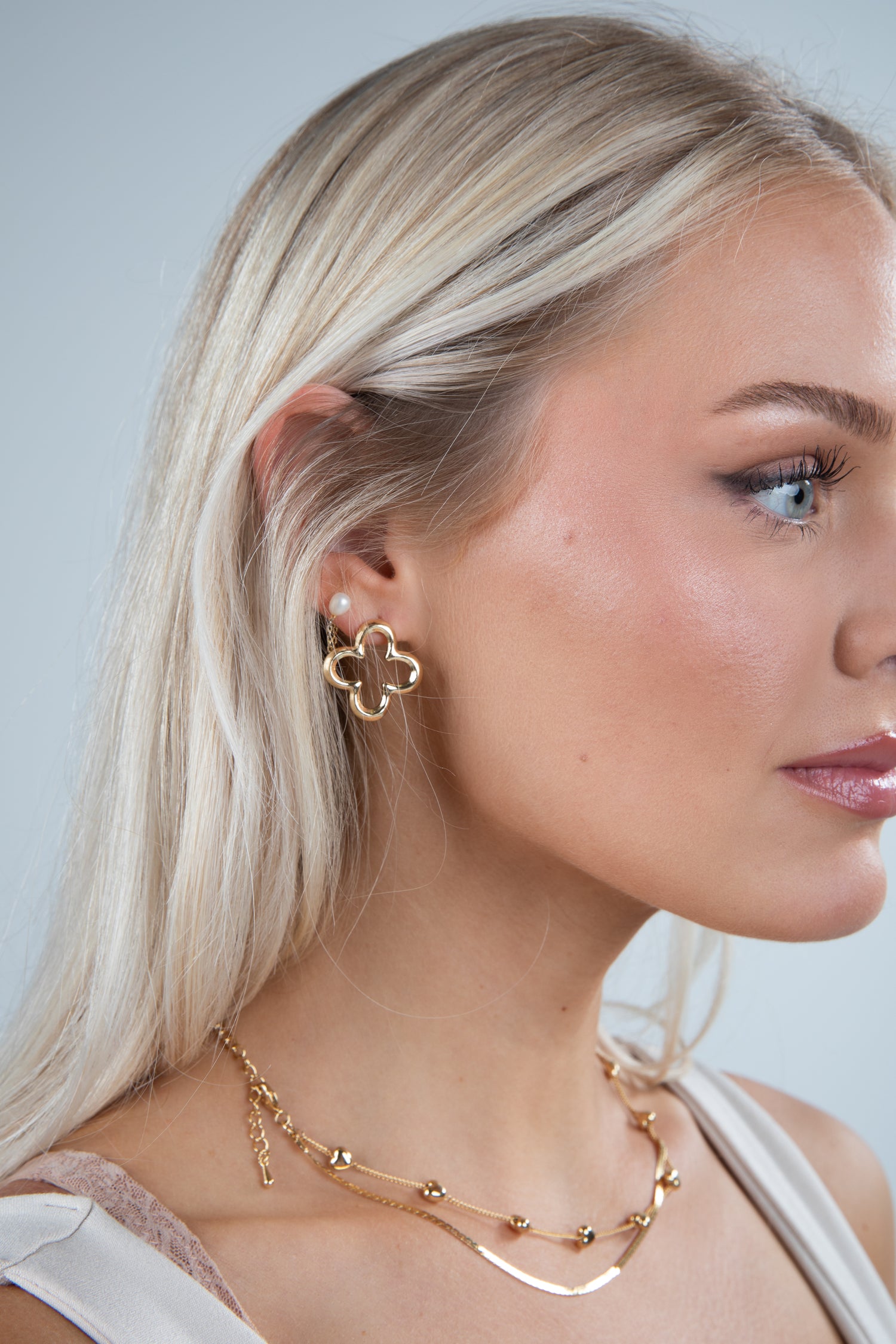 Woman wearing gold earrings and necklace against a light gray background