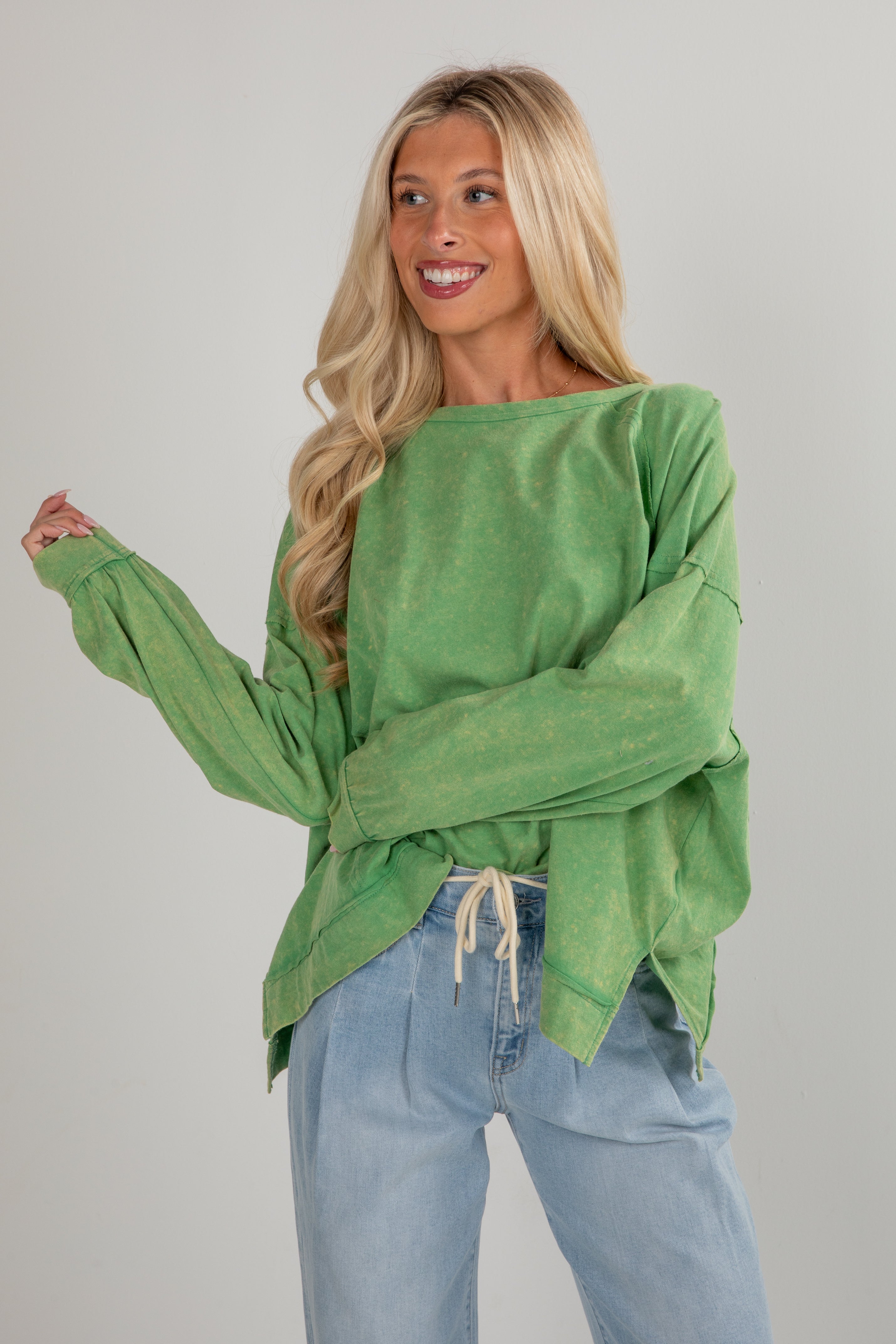 Woman wearing a green oversized sweater and blue jeans against a gray background