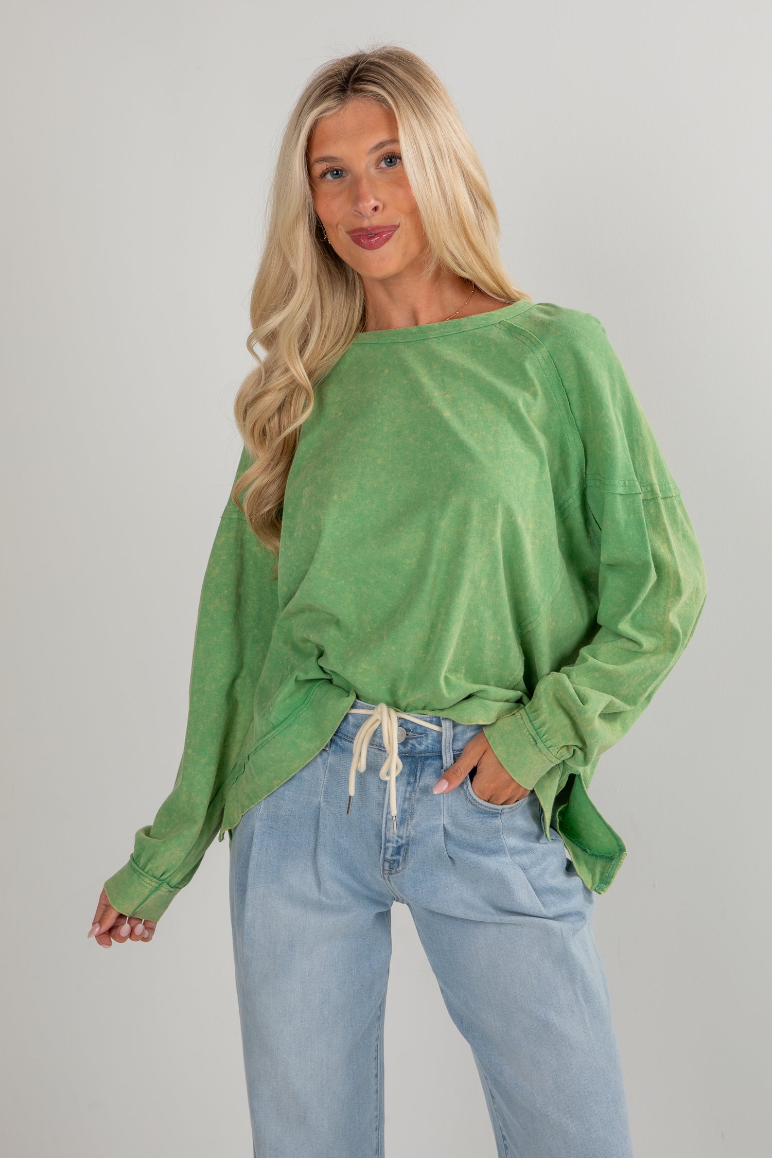 Woman wearing a green oversized sweatshirt and blue jeans against a plain background