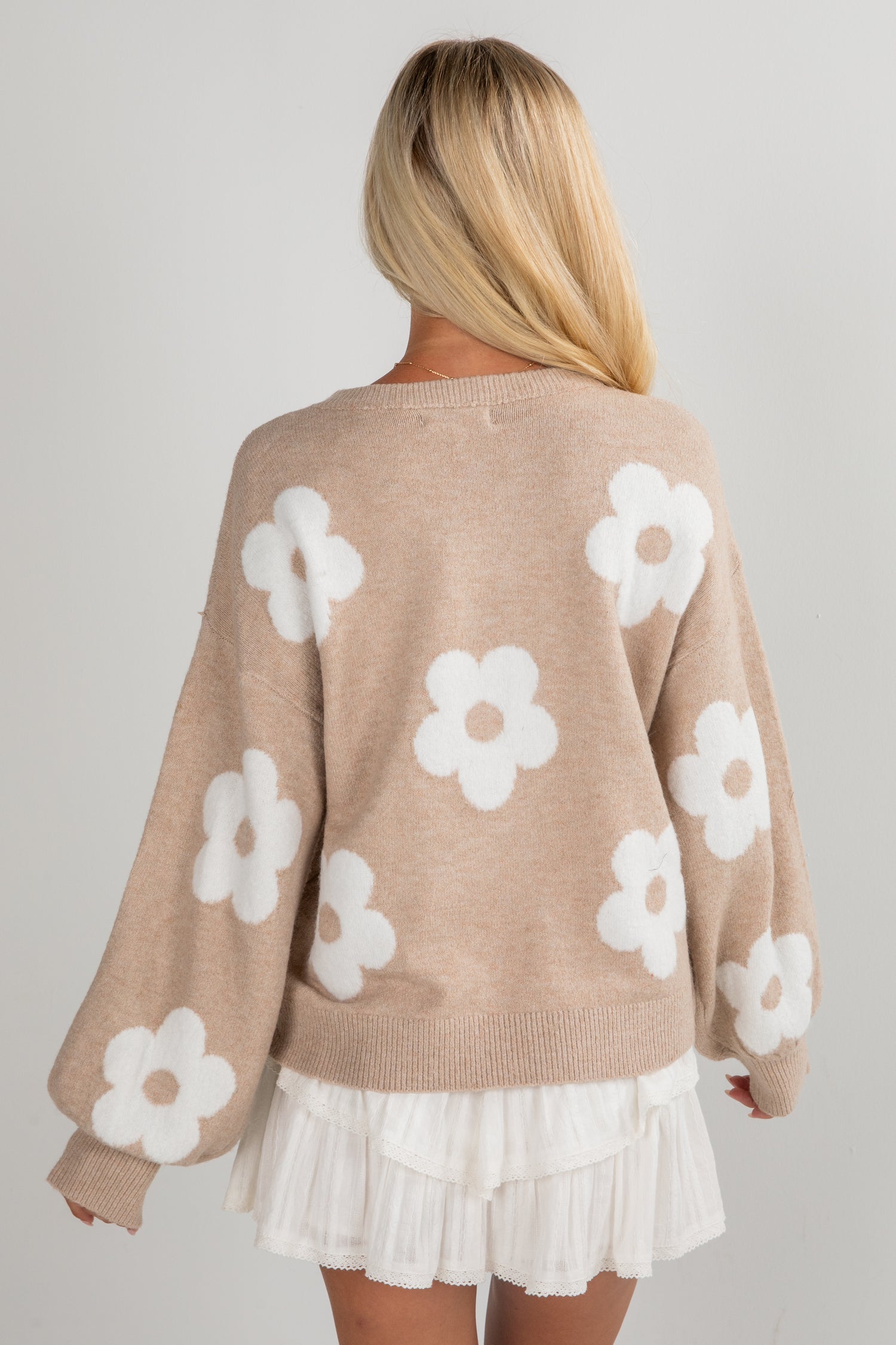 Beige sweater with white floral patterns worn by a person on a plain background