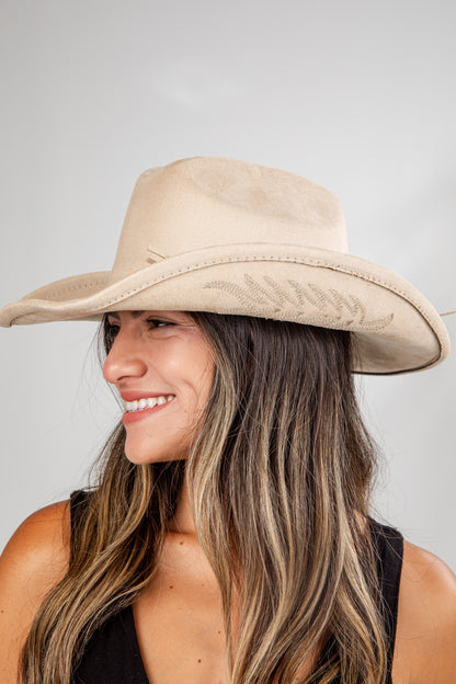 Woman wearing a beige wide-brimmed hat against a plain background