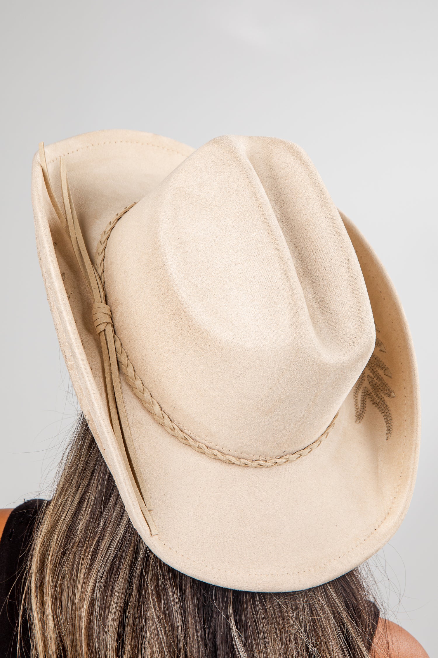 Beige fedora hat worn by a person with a plain background