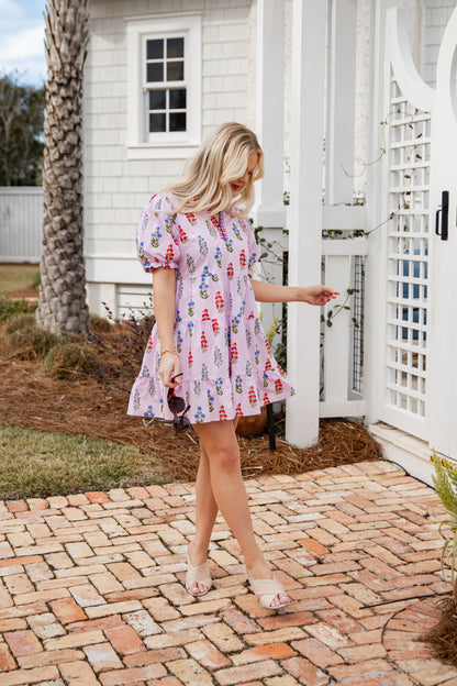 Woman in a patterned dress standing on a brick path in front of a white building.