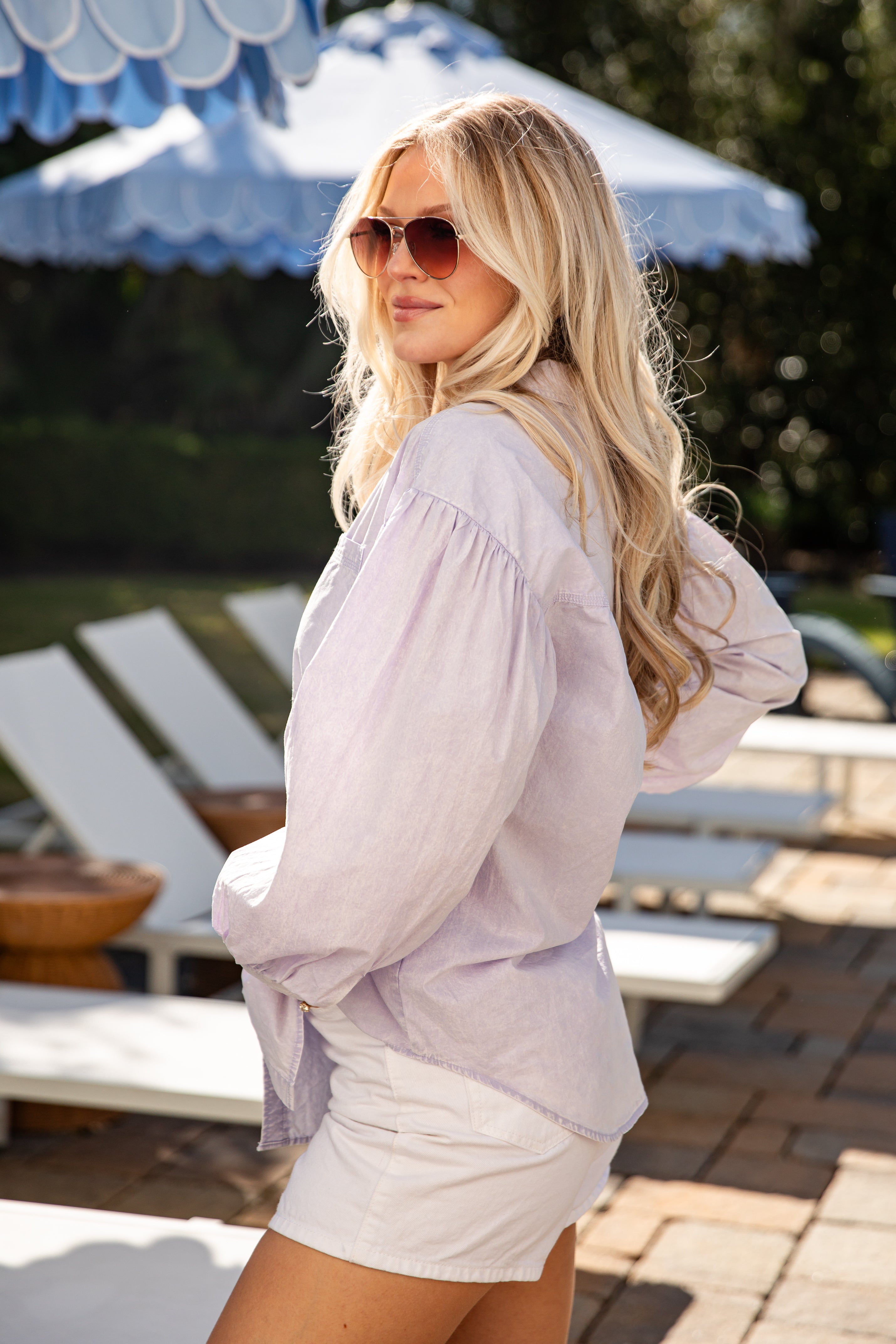 Woman in a light blouse and shorts standing by lounge chairs with umbrellas in the background