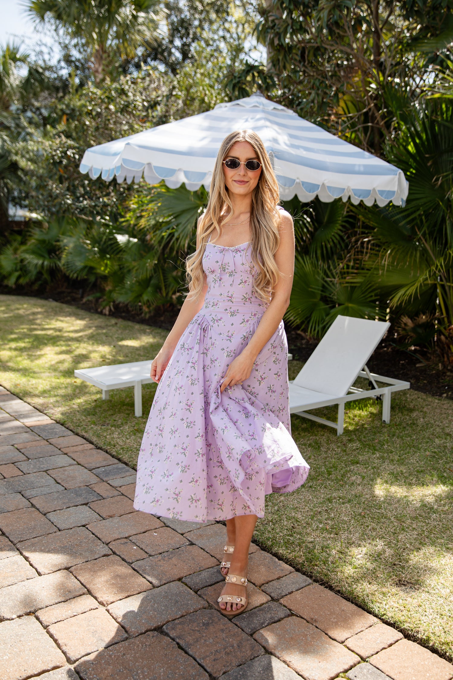 Woman in a floral dress standing under a striped umbrella in a garden setting