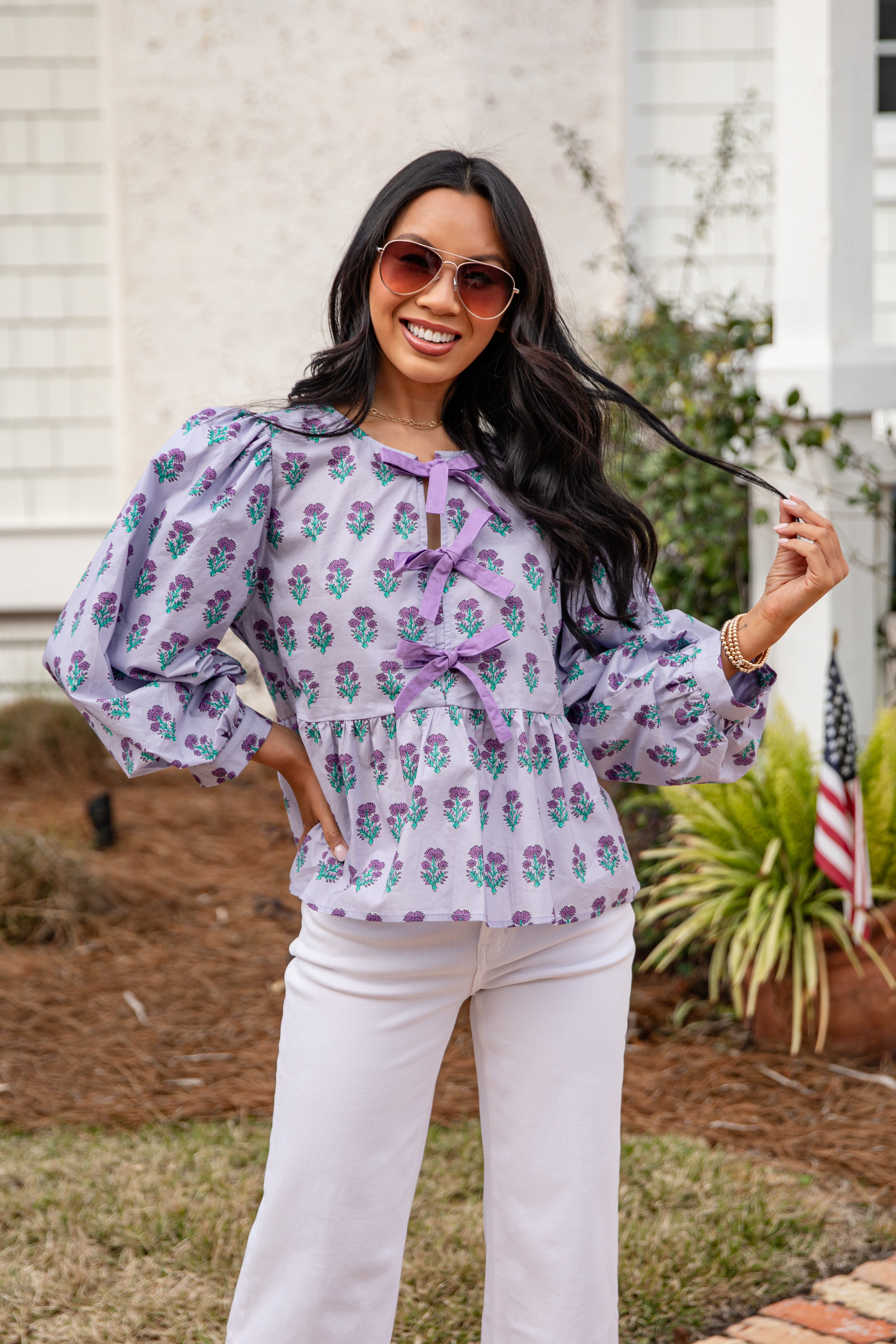 Woman wearing a floral blouse and white pants outdoors.