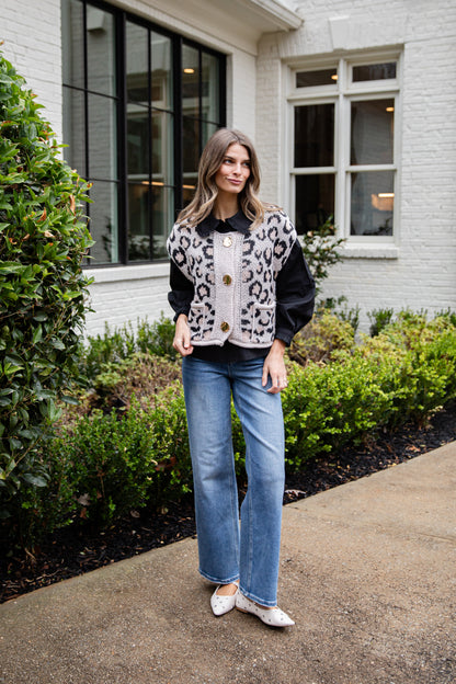 Woman wearing a leopard print jacket and blue jeans standing outside a building.