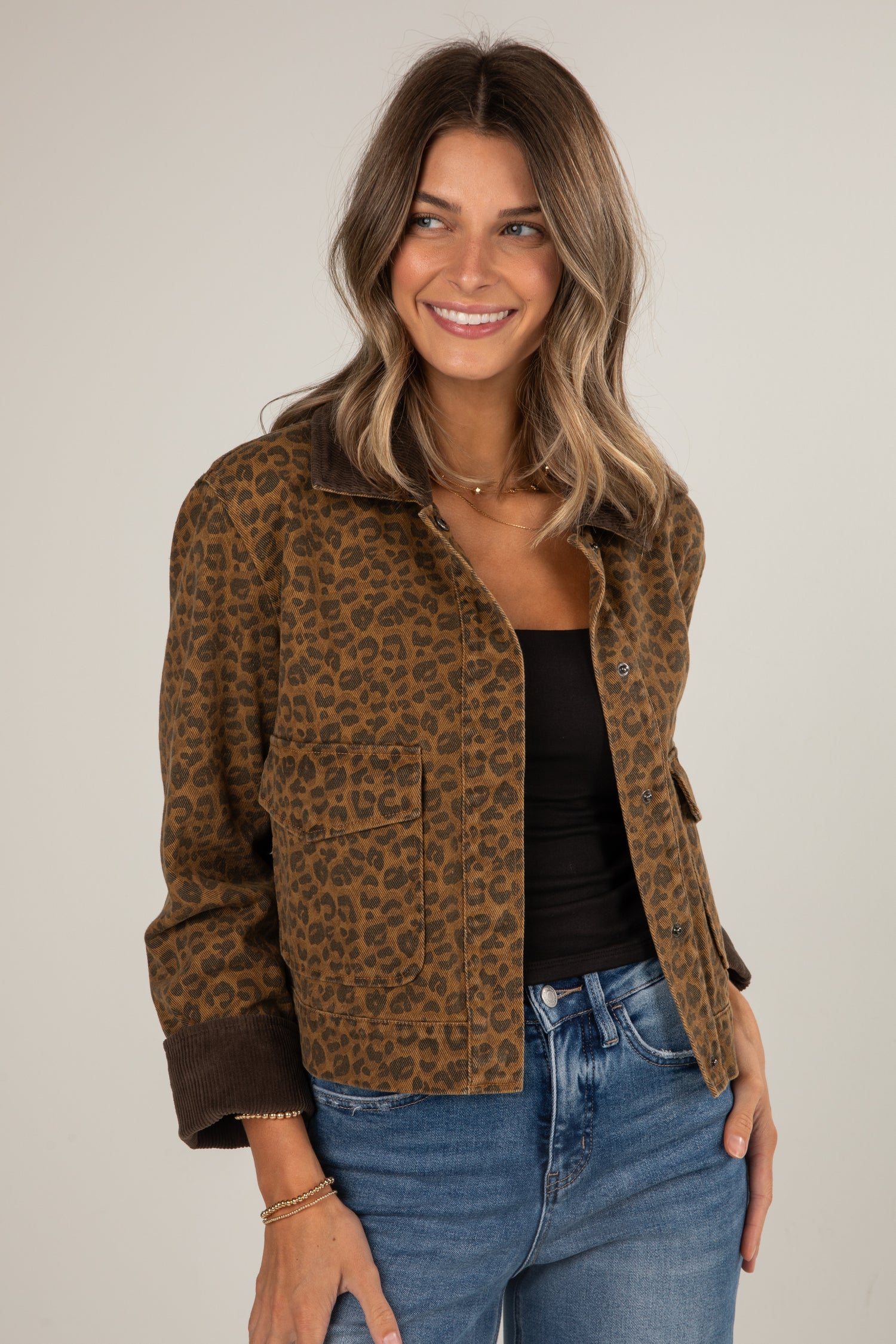 Woman wearing a leopard print jacket, black top, and blue jeans on a plain background