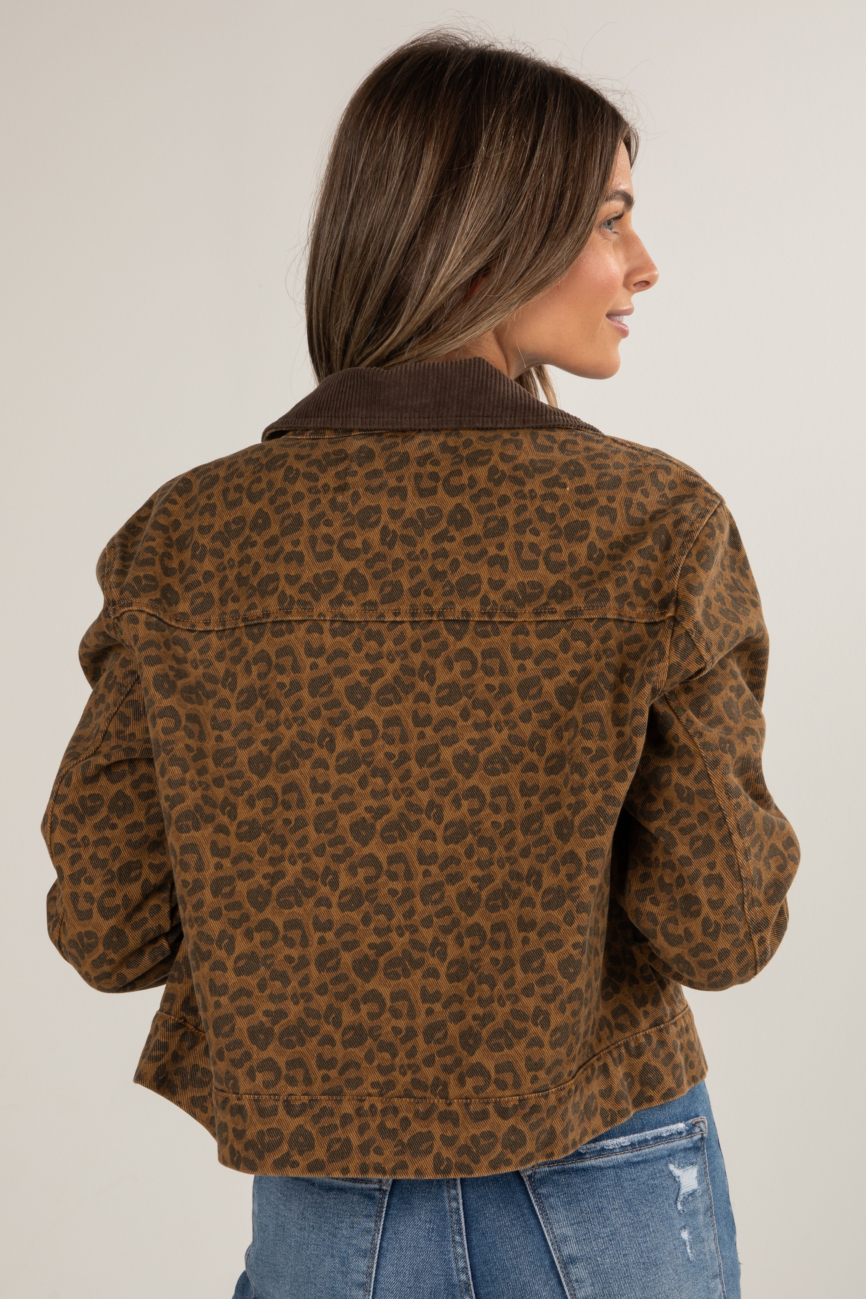 Woman wearing a brown leopard print jacket and blue jeans on a white background