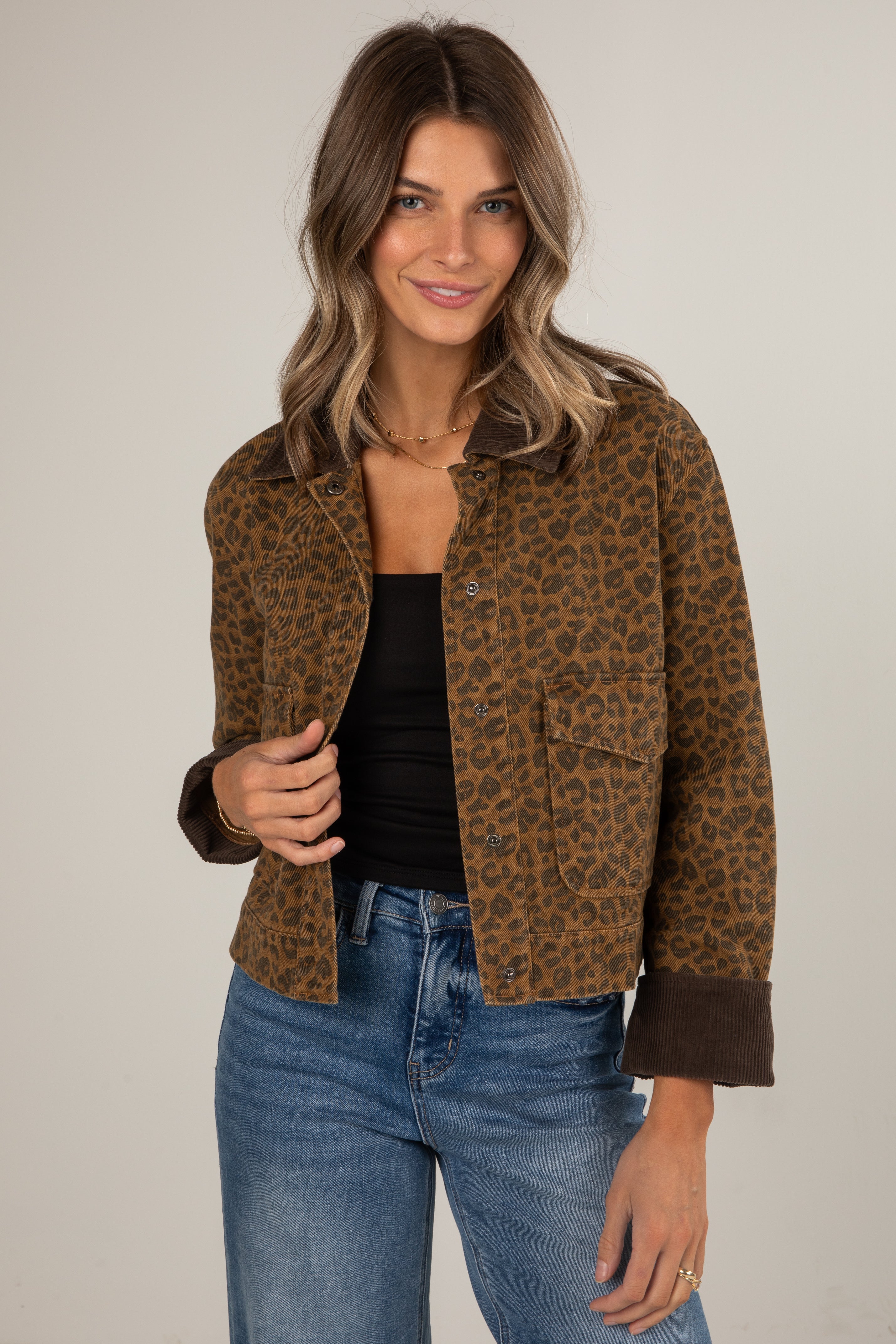 Woman wearing a leopard print jacket and blue jeans on a plain background